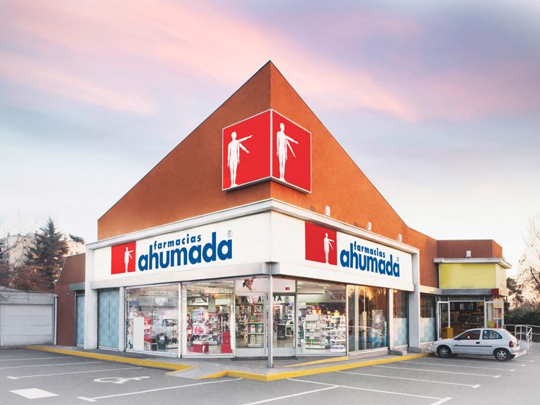 Farmacéutico atendiendo a un cliente en el mesón de una farmacia, con estantes de medicamentos al fondo