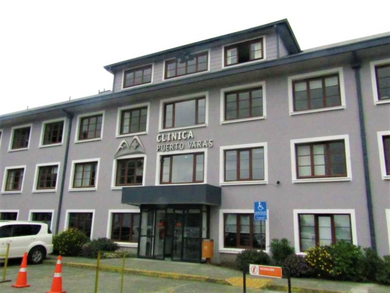 Pasillo interior de una clínica moderna con personal médico en movimiento y señalética hospitalaria visible en Puerto Varas, Chile