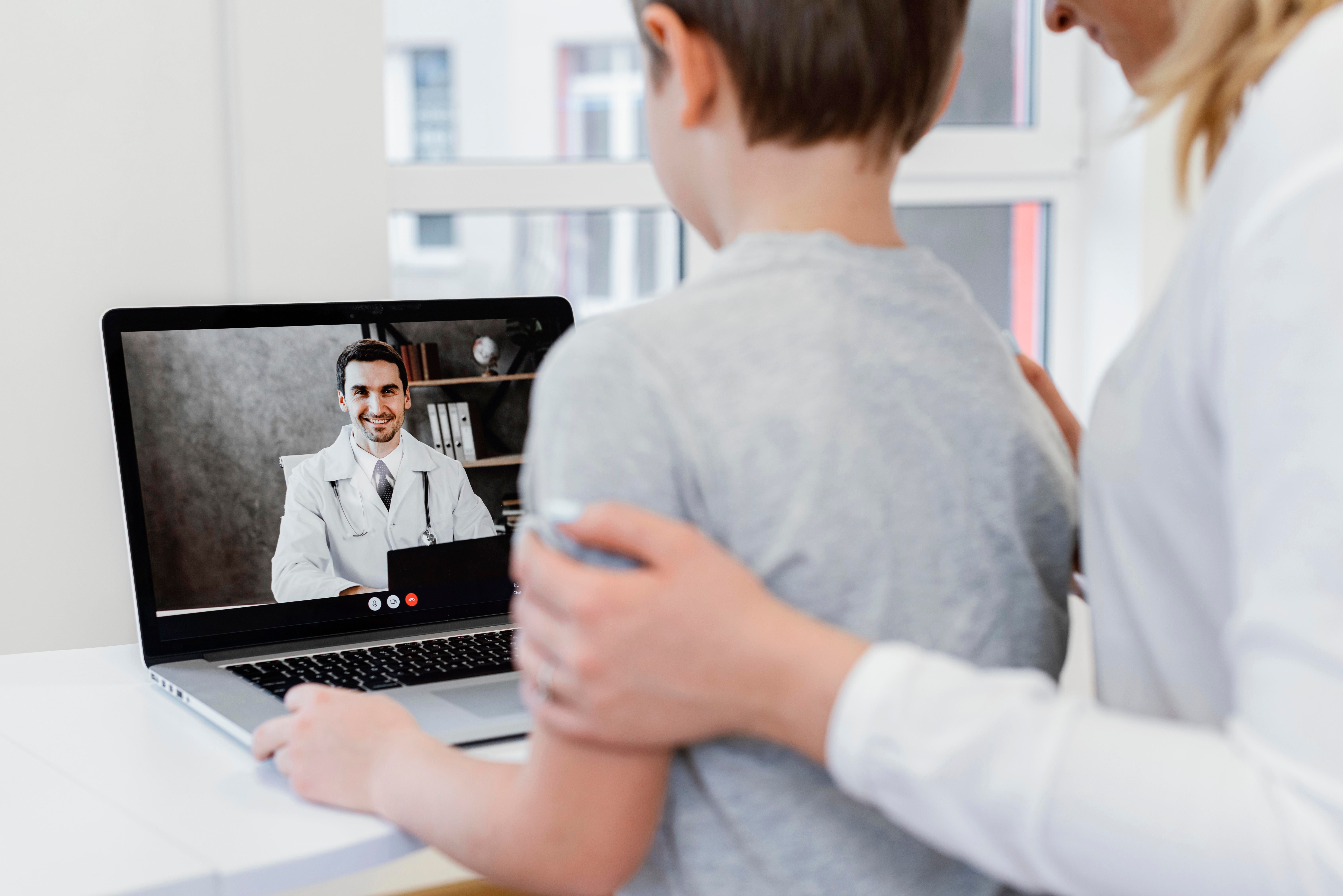 Médico en videollamada con paciente desde su domicilio, con aplicación móvil de telemedicina en primer plano